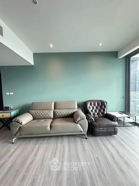 Modern living room with stylish sofa and armchair, featuring sleek flooring and a calming green accent wall.