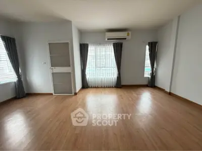 Spacious empty room with wooden flooring and large windows, perfect for customization.