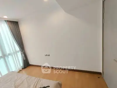 Spacious bedroom with wooden flooring and large window for natural light.