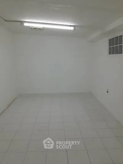 Spacious white-tiled room with bright fluorescent lighting, ideal for storage or utility use.