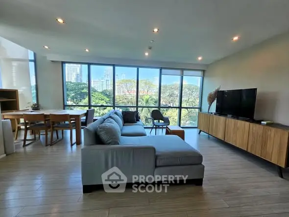 Spacious modern living room with large windows offering stunning city and park views, featuring stylish furniture and open layout.