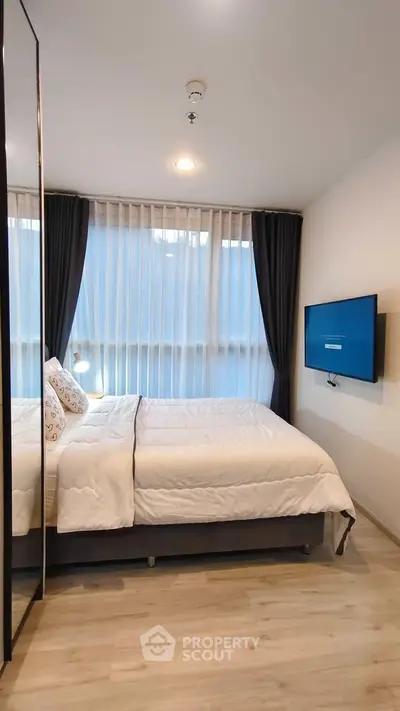 Modern bedroom with large window and wall-mounted TV in stylish apartment.