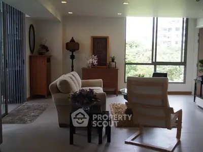 Spacious living room with modern furniture and large window offering a lush green view.