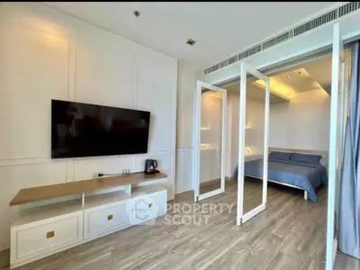 Modern apartment interior with sleek TV setup and cozy bedroom, featuring elegant wooden flooring.