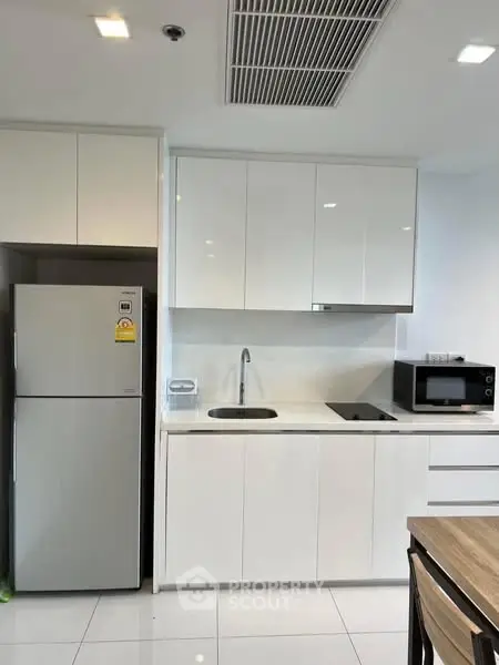 Modern kitchen with sleek white cabinets and appliances, including fridge and microwave, in a bright setting.