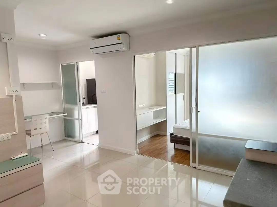 Modern apartment interior with open layout, featuring a study area and sliding glass doors to bedroom.
