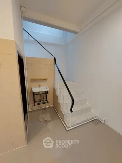 Pristine white-tiled bathroom with modern fixtures and a unique staircase leading to an upper level, showcasing a clever use of space in a stylish home.