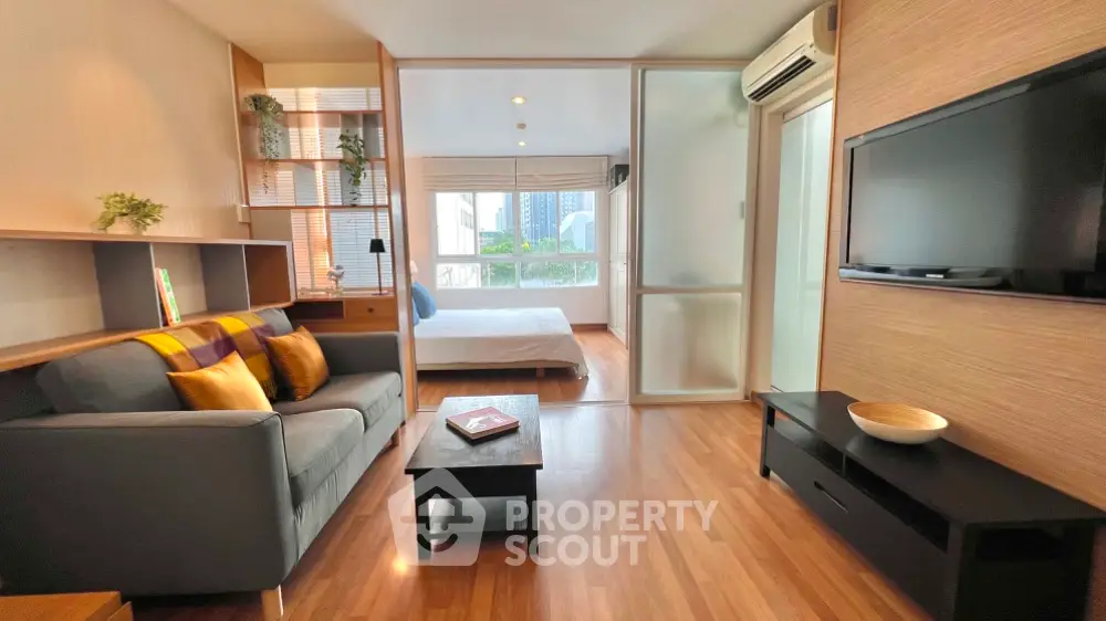 Modern open-plan living room with cozy seating and stylish decor, leading to a bright bedroom with city views.