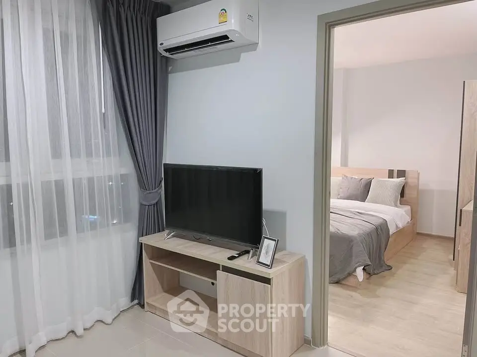 Modern living room with TV and air conditioning, leading to a cozy bedroom with stylish decor.