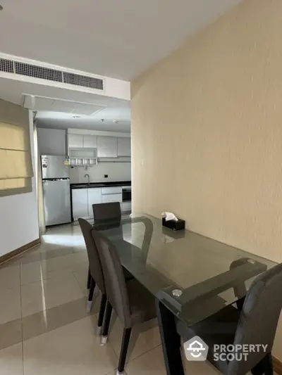 Modern dining area with glass table and kitchen view in stylish apartment