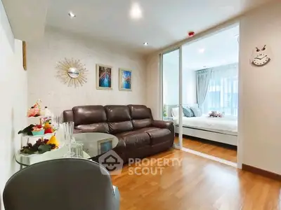 Modern living room with leather sofa and glass table, adjacent to a cozy bedroom with natural light.