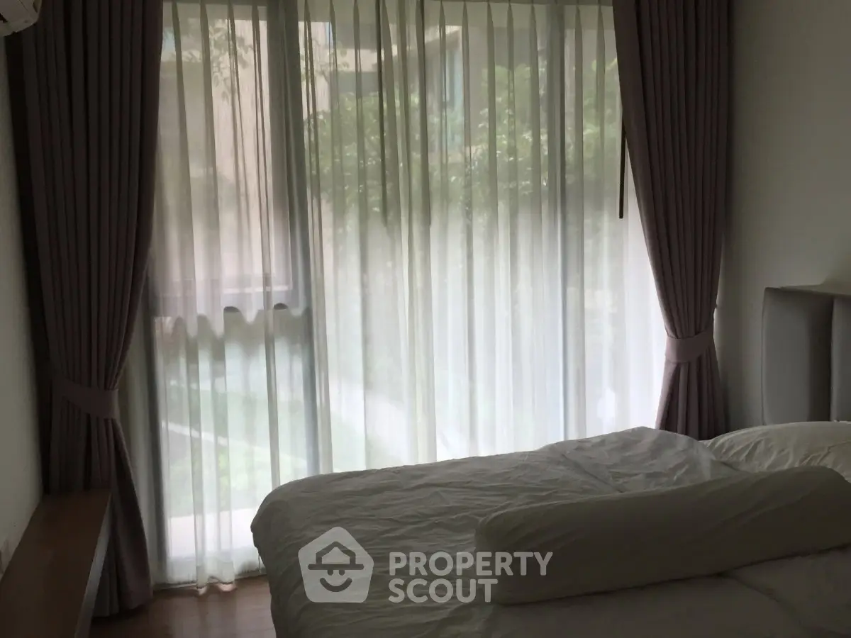 Cozy bedroom with large window and elegant curtains overlooking lush greenery.