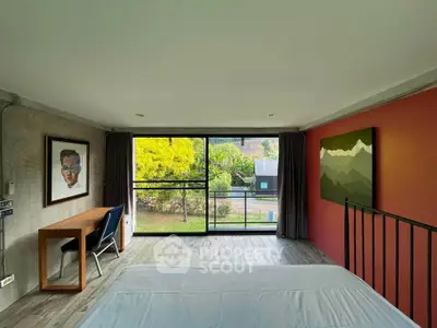 Spacious bedroom with large window offering scenic garden view, modern decor, and cozy workspace.