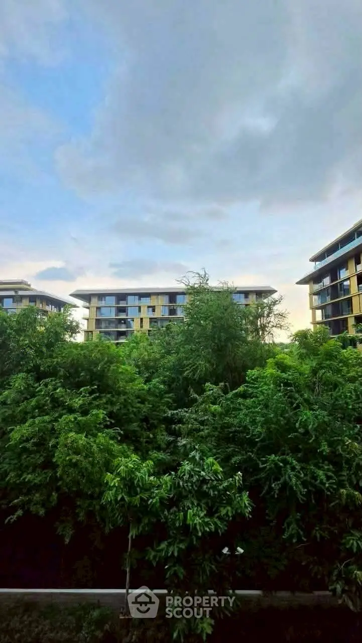 Modern residential buildings surrounded by lush greenery under a cloudy sky, offering serene living environment.