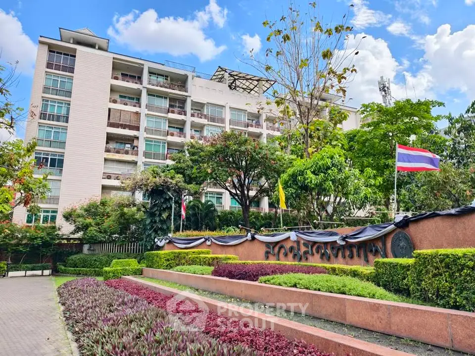 Modern apartment building with lush gardens and national flags, offering a serene urban living experience.