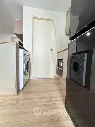 Modern kitchen with sleek appliances and washing machine, featuring light wood flooring.