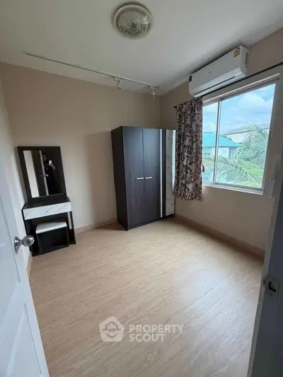 Spacious bedroom with wooden flooring, wardrobe, and large window with scenic view.