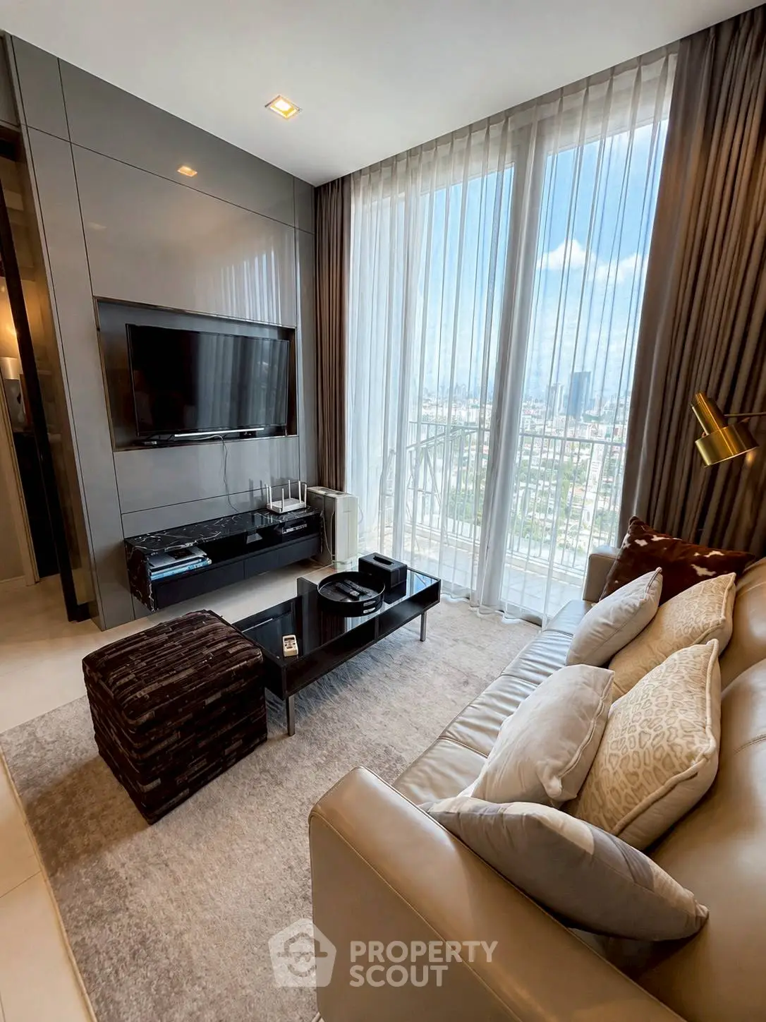 Luxurious living room with floor-to-ceiling windows and city view, featuring modern decor and plush seating.