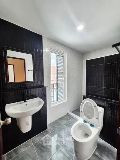 Modern bathroom with sleek black and white tiles, featuring a toilet and sink under bright lighting.