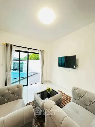 Modern living room with pool view, featuring elegant furniture and wall-mounted TV.