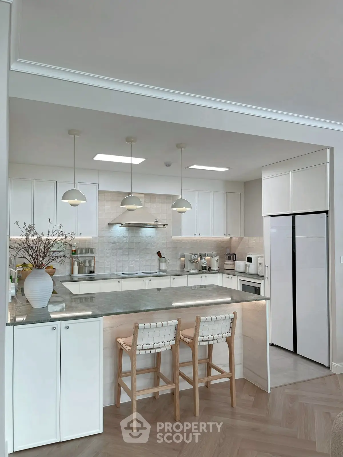 Modern kitchen with sleek white cabinets, island seating, and contemporary lighting fixtures.