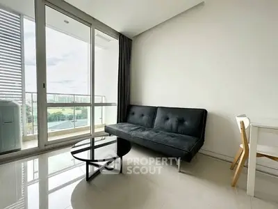Modern living room with sleek black sofa and glass coffee table, featuring a large balcony with city view.