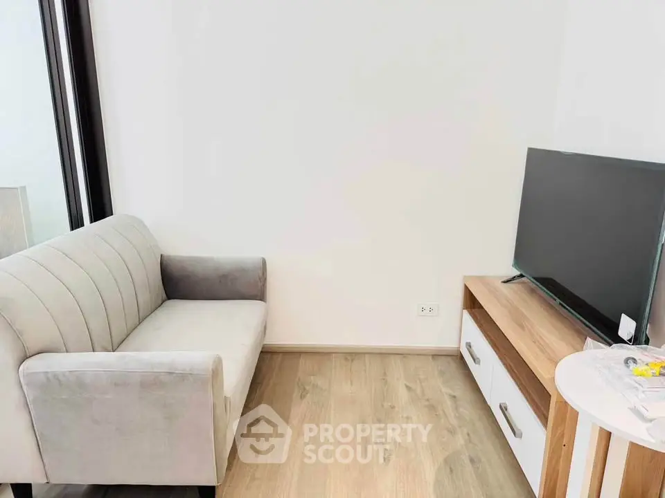 Modern living room with sleek sofa and flat-screen TV on wooden stand.
