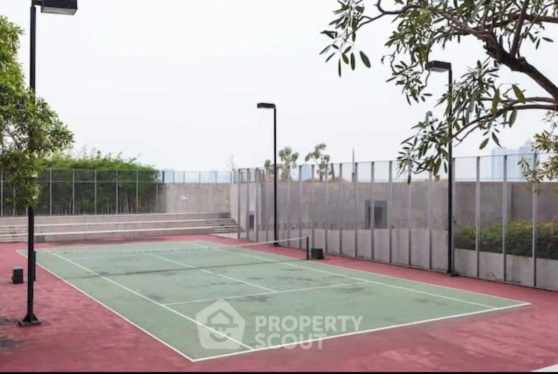 Spacious outdoor tennis court with modern fencing and lush greenery, perfect for sports enthusiasts.
