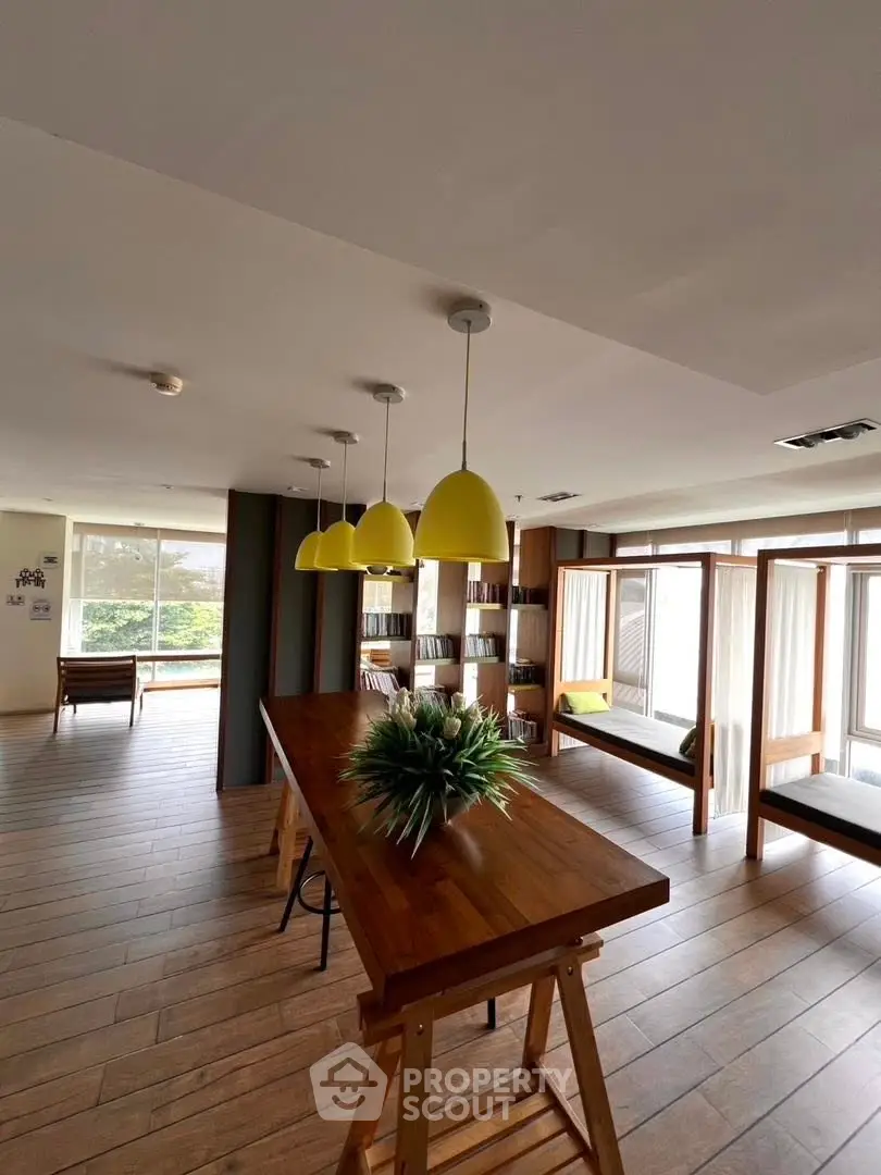 Spacious modern living area with wooden floors, large windows, and stylish pendant lighting.
