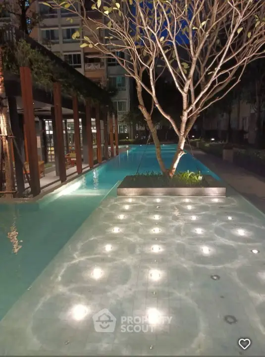Luxurious apartment complex with illuminated pool and modern landscaping at night.