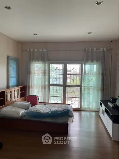 Spacious bedroom with large windows and modern furnishings, offering ample natural light and a cozy atmosphere.