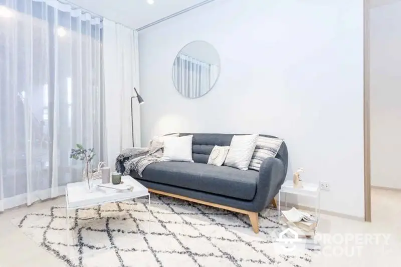 Elegant minimalist living room with a chic black sofa, stylish rug, and modern accents, bathed in natural light from the sheer curtains.