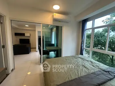 Modern bedroom with large windows and view of greenery, connected to living area with glass sliding doors.