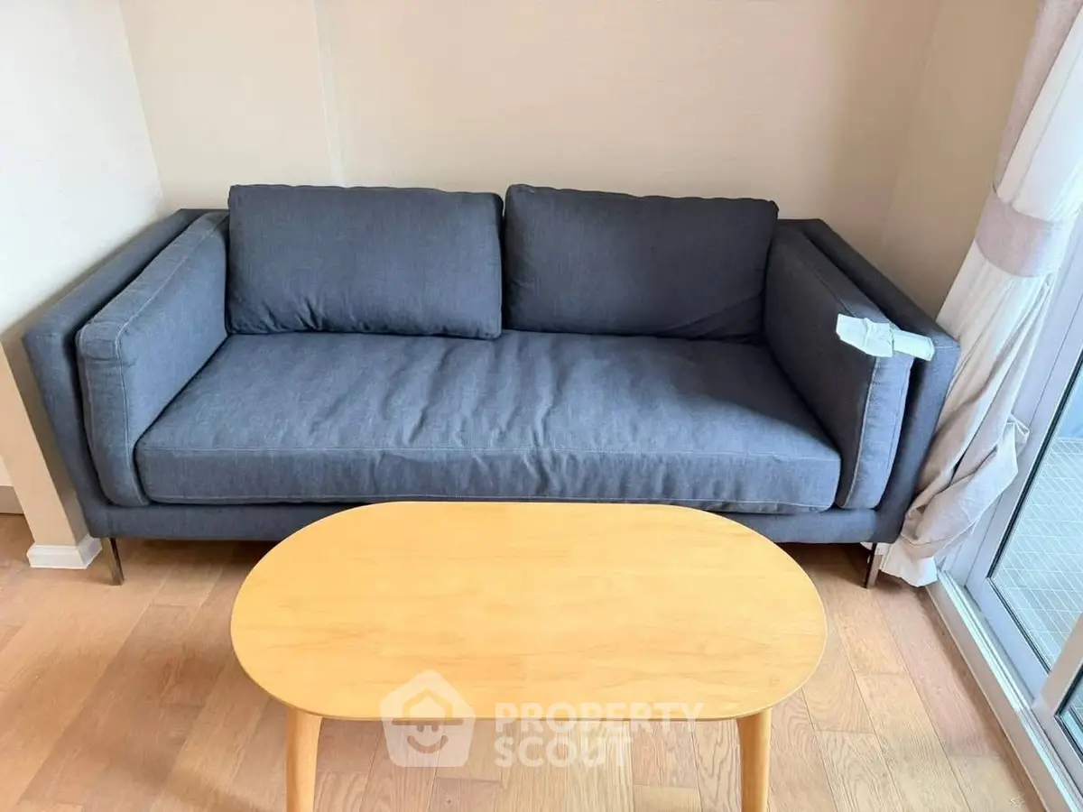 Modern living room with stylish gray sofa and wooden coffee table near large window.