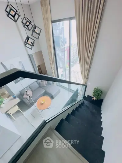 Modern duplex interior with stylish staircase and large windows offering city views.