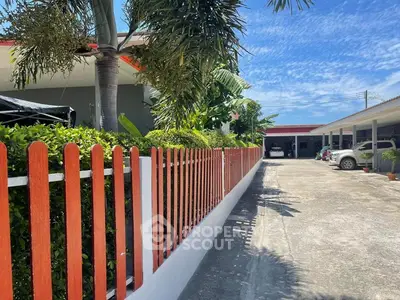 Charming residential property with vibrant red fence and lush greenery under a clear blue sky.