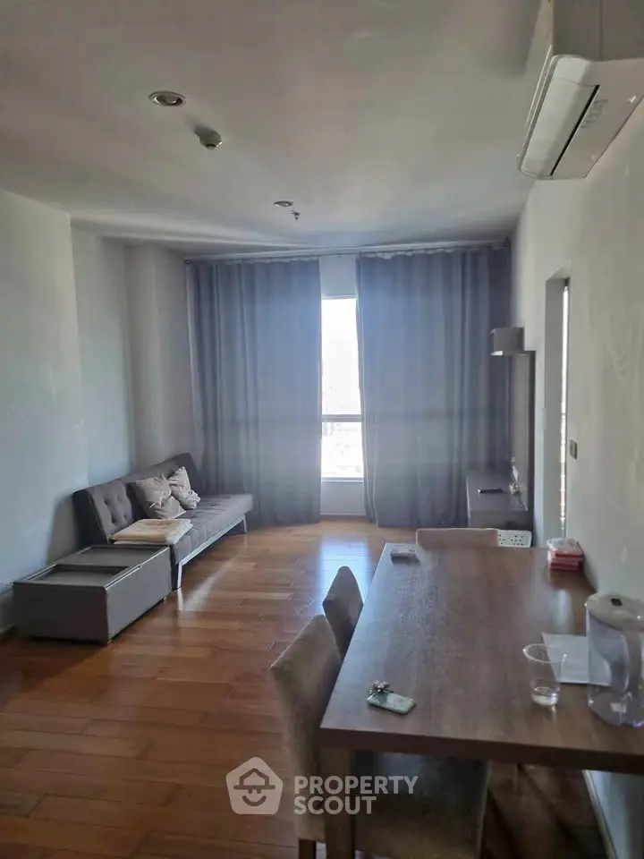 Cozy living room with wooden flooring and modern furniture, featuring a large window with curtains.