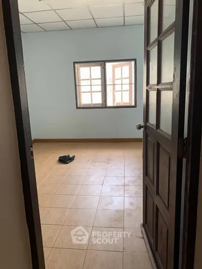 Spacious empty room with tiled flooring and large window, perfect for customization.