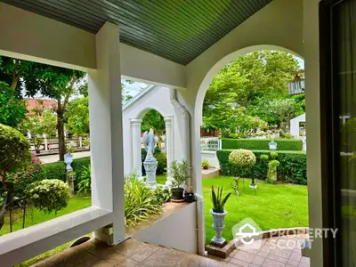 Charming garden view from elegant covered patio with lush greenery and classic white archway.