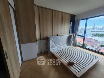 Modern bedroom with wooden flooring and large window offering city view, featuring a sleek bed frame.