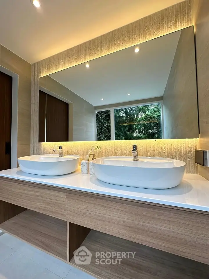 Luxurious modern bathroom with dual sinks and large mirror, featuring elegant lighting and natural views.