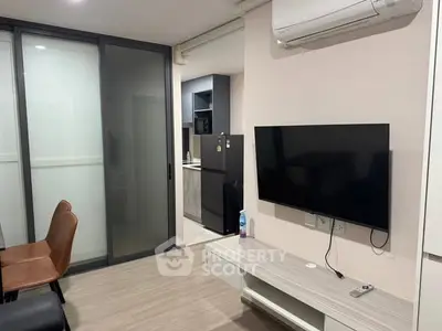 Modern living room with wall-mounted TV and sliding glass doors leading to kitchen.
