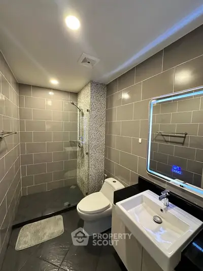 Modern bathroom with sleek tiles and illuminated mirror in a contemporary home.