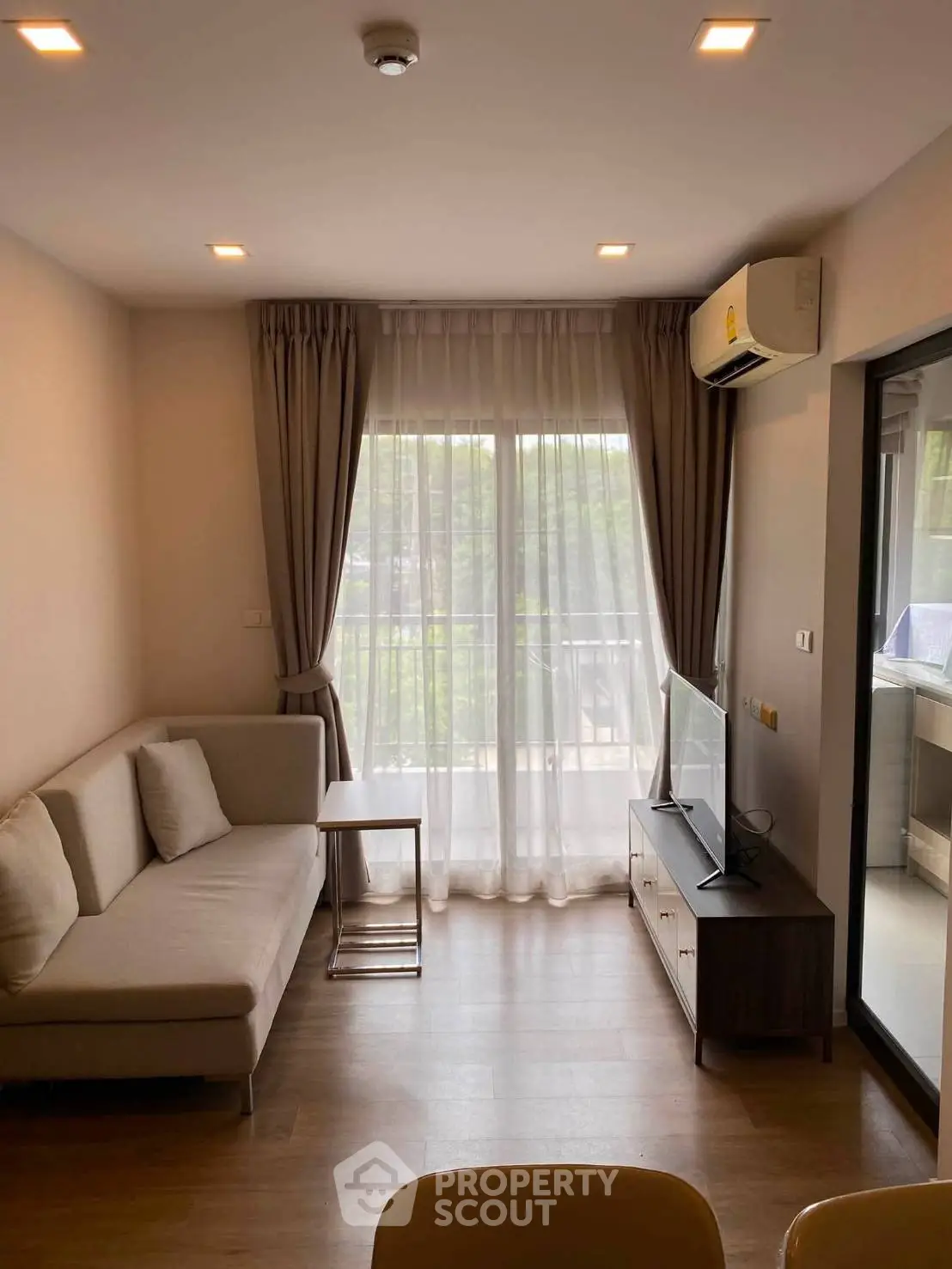 Modern living room with cozy sofa, TV, and balcony view, perfect for relaxation.