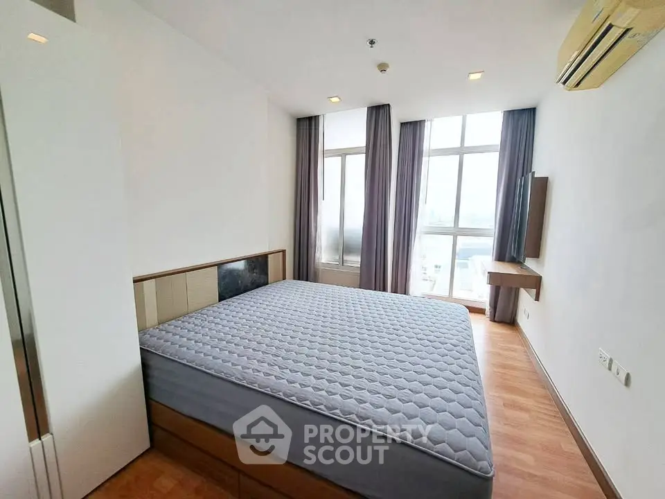 Spacious bedroom with large window and modern furnishings in a high-rise apartment.
