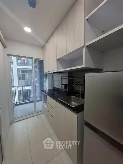 Modern kitchen with sleek cabinetry and balcony view in urban apartment.