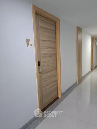 Modern apartment hallway with sleek wooden doors and polished flooring.