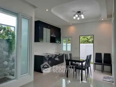 Modern kitchen with sleek black cabinets and dining area, featuring large windows and stylish lighting.