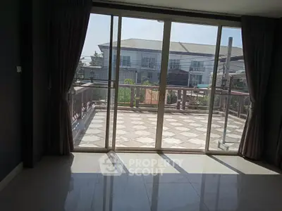 Spacious room with large sliding glass doors leading to a sunlit balcony with a view of modern houses.