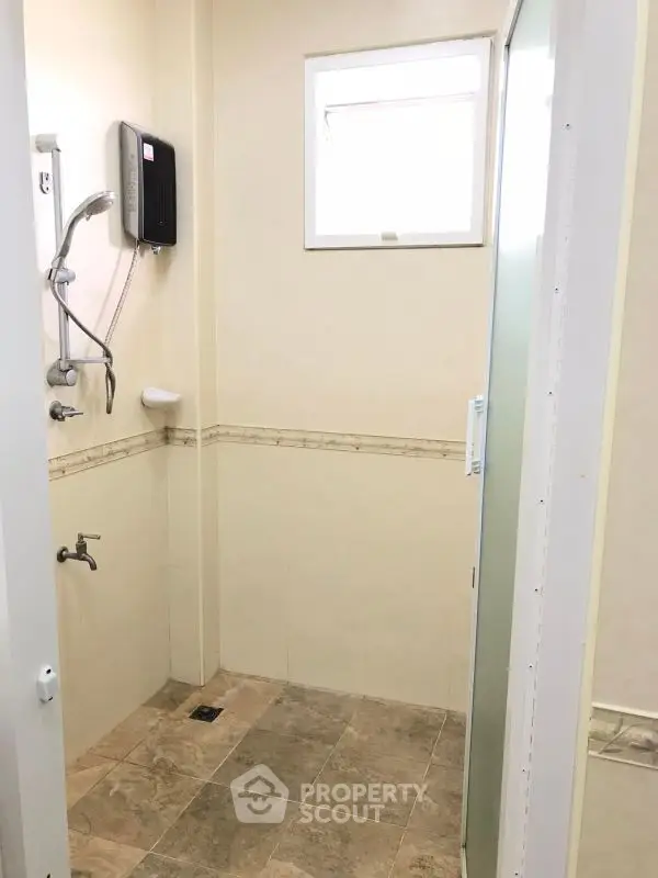Compact bathroom with shower and tiled floor, featuring neutral tones and a small window for natural light.